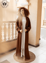 Woman wearing a brown designer abaya with white piping details on a balcony, modest fashion UAE
