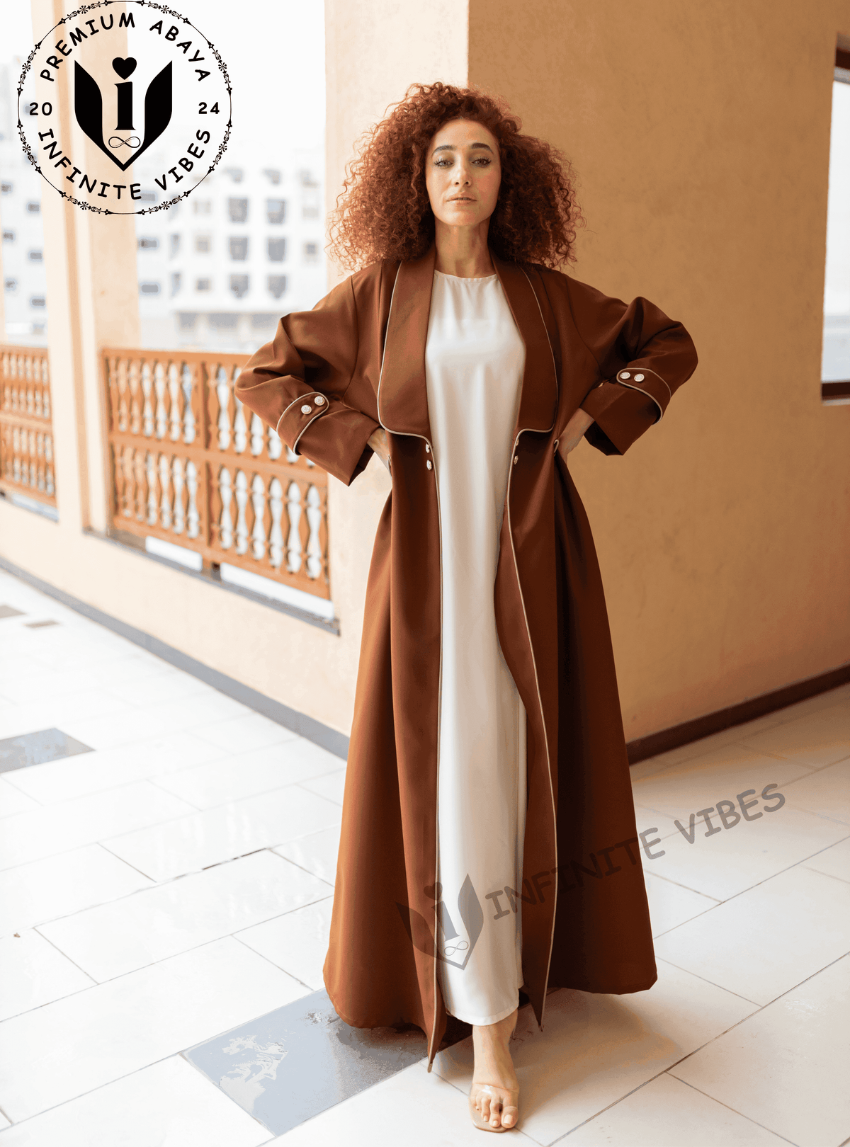 Woman modeling a brown designer abaya with white trim, standing on a balcony in Dubai.