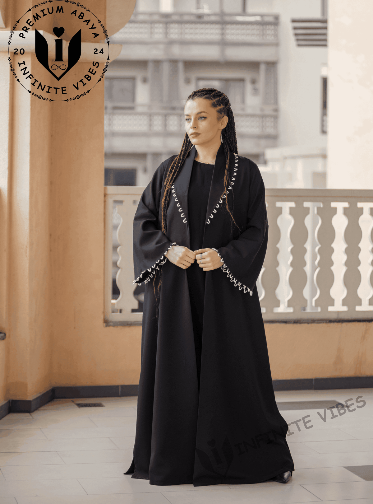 Woman wearing a premium black designer abaya with white trim, standing on a balcony.