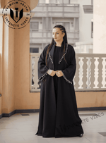 Woman wearing a premium black designer abaya with white trim, standing on a balcony.