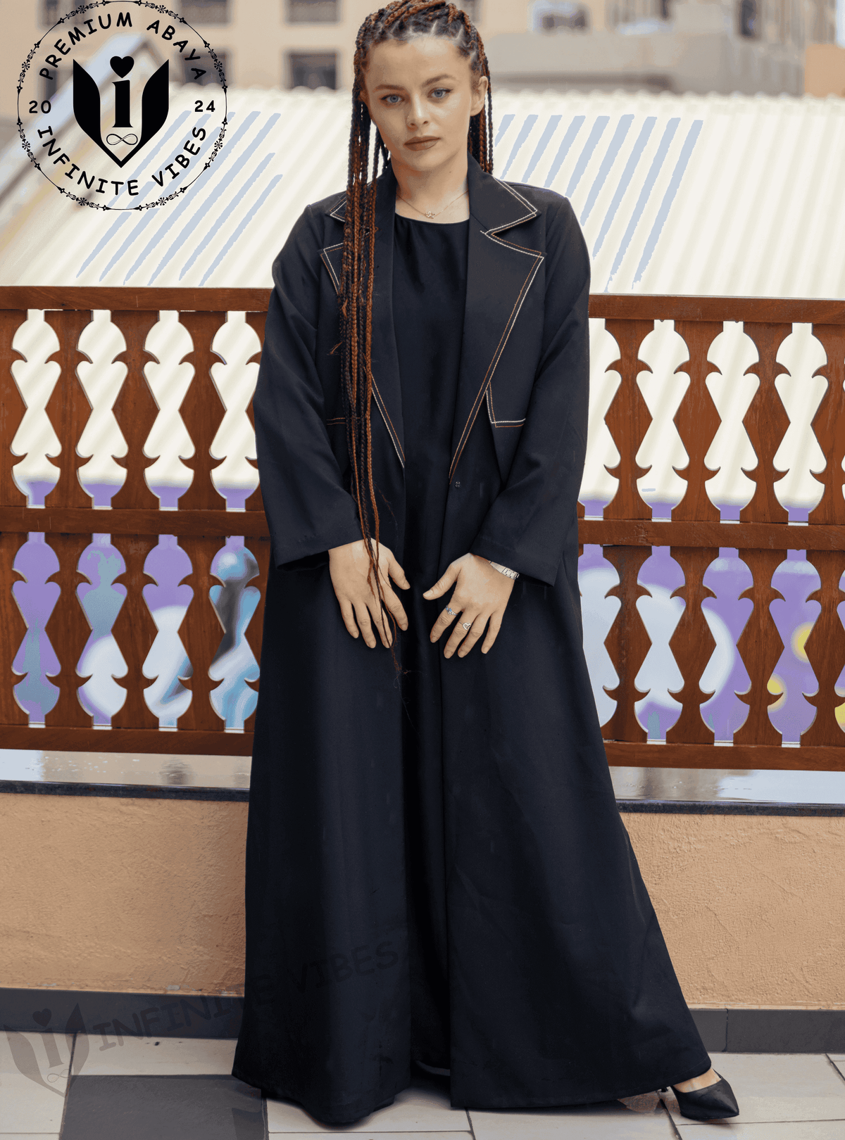 Woman wearing a black designer abaya with contrast stitching on balcony, modest fashion UAE