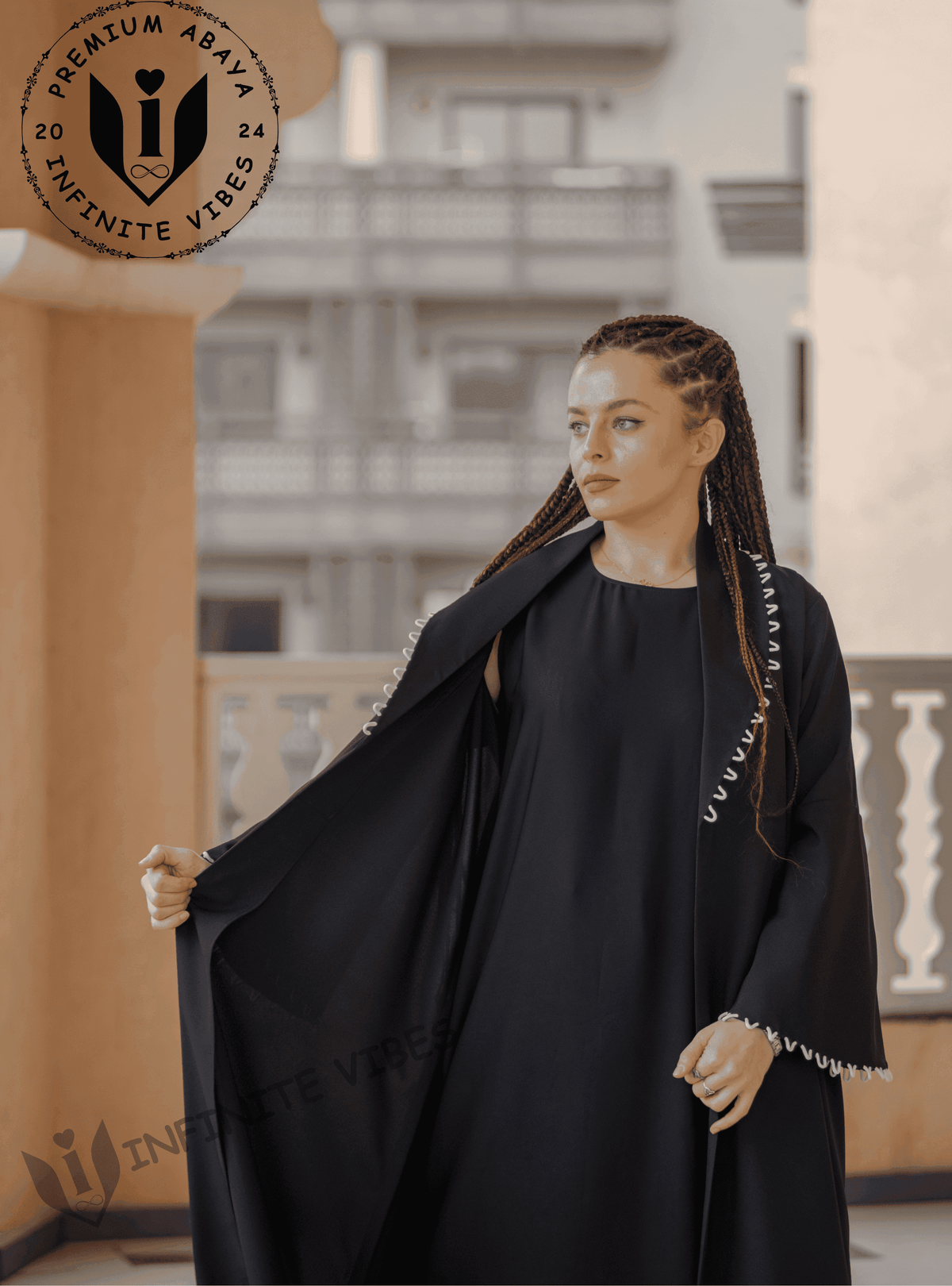 Woman wearing a black designer abaya with white trim, standing on a balcony