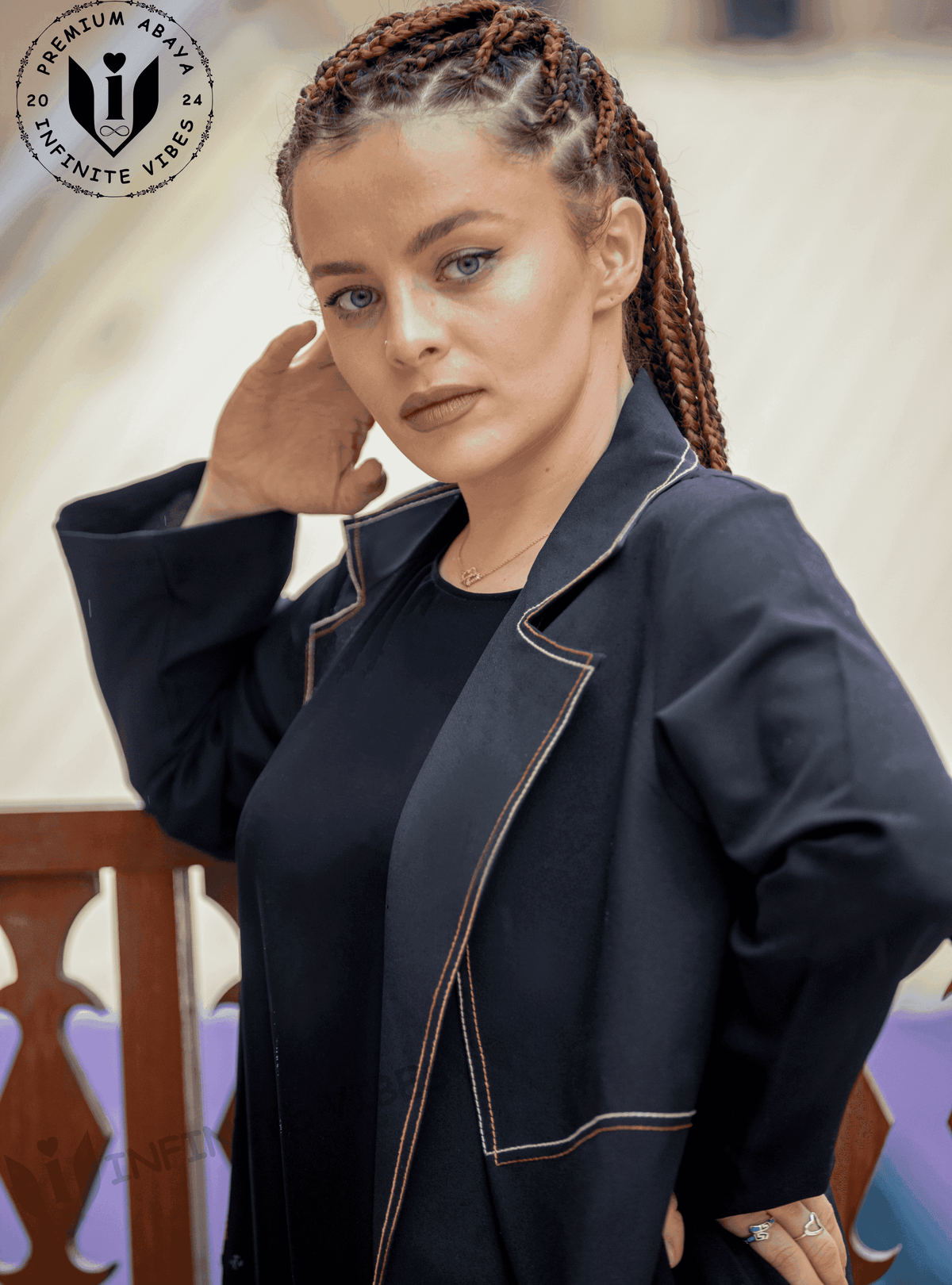 Woman with braided hair modeling a black designer abaya with beige contrast stitching.