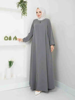 Woman wearing a grey modest abaya with white hijab in a minimalist room