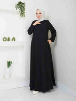 Woman in a simple black abaya and white hijab standing in a modern minimal room.