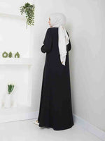 Woman wearing a black abaya and light hijab, standing in minimal modern room