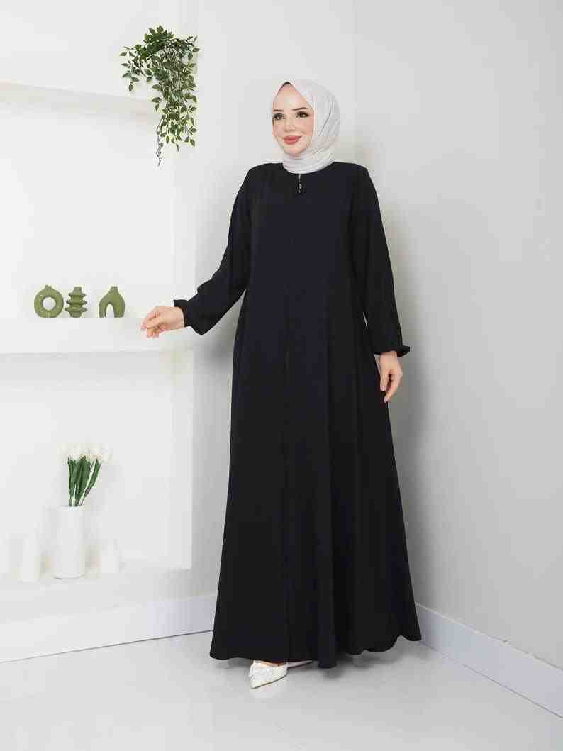Woman in a black abaya with white hijab, modest fashion, standing in modern interior