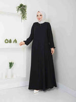Woman in a black abaya with white hijab, modest fashion, standing in modern interior
