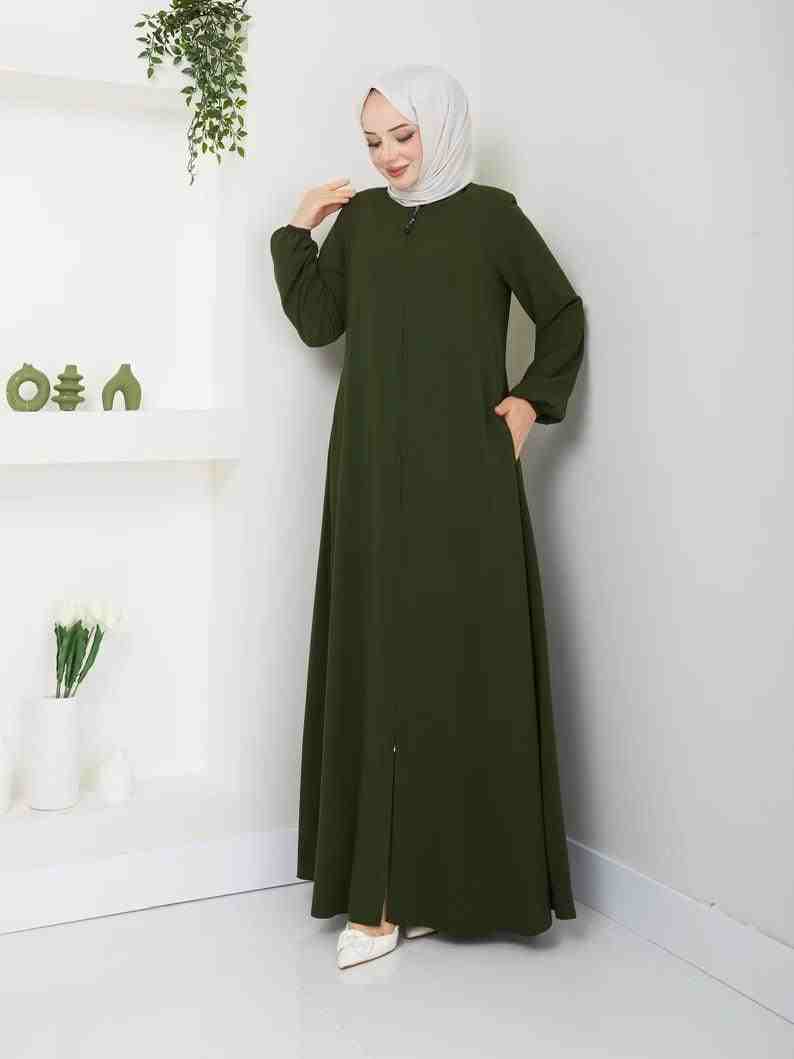 Woman in olive green abaya and white hijab standing indoors, modest fashion