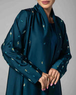 Woman wearing a teal embellished abaya with gold and blue accents, modest fashion style
