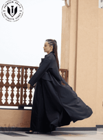 Woman wearing a flowing black designer abaya on a balcony, modest fashion style.