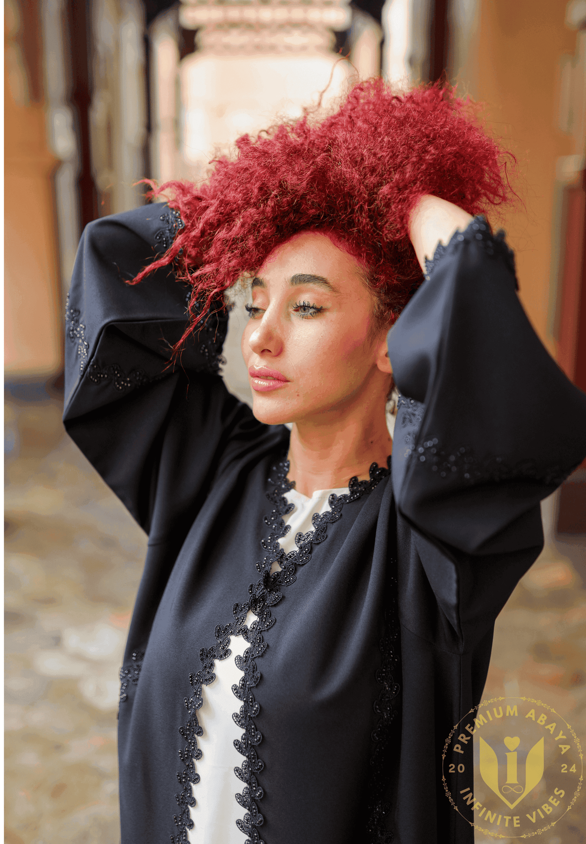 Woman with curly red hair wearing a black embroidered abaya, outdoor setting