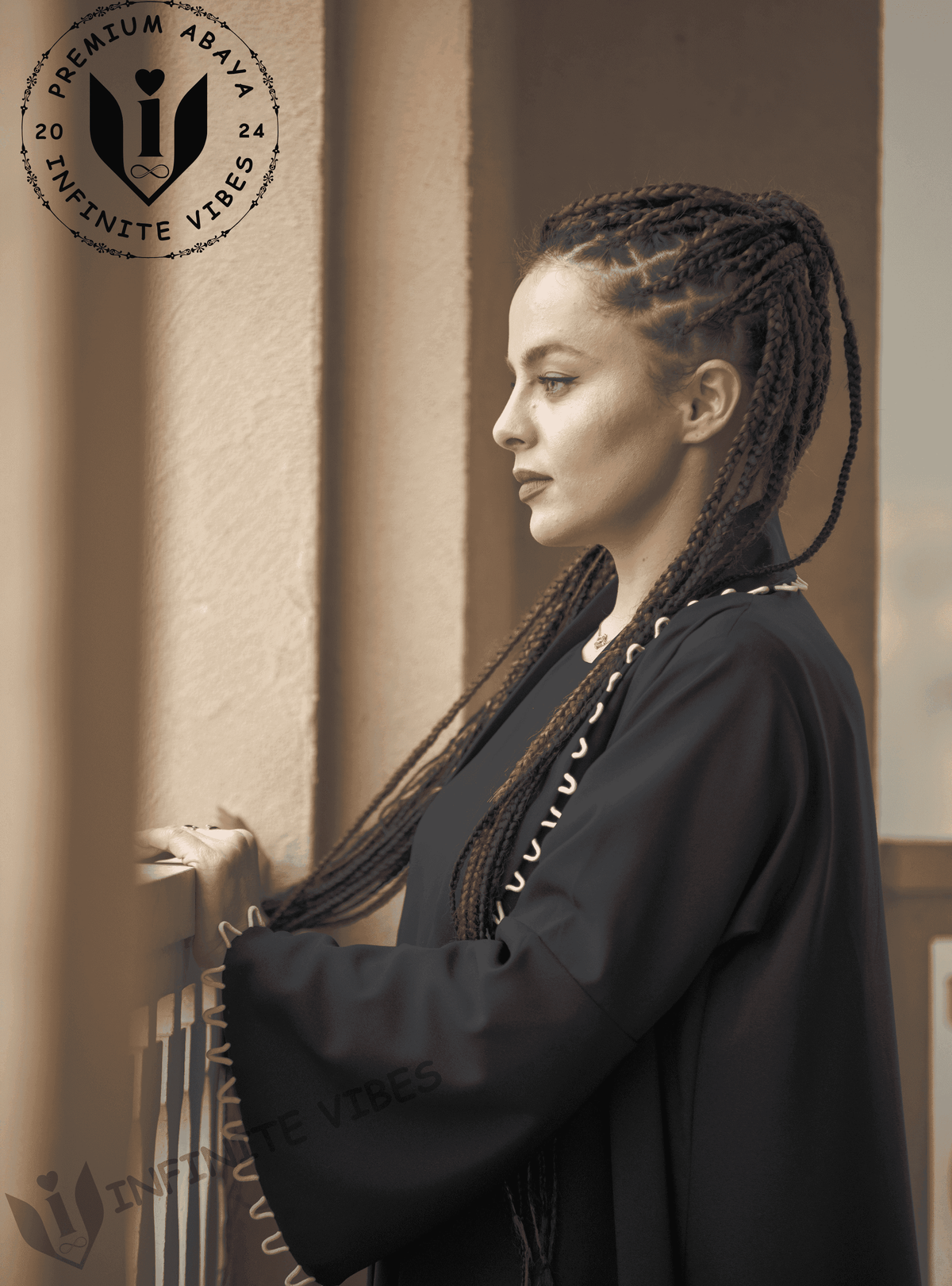 Woman in modern black designer abaya with braided hair, standing on a balcony, UAE fashion