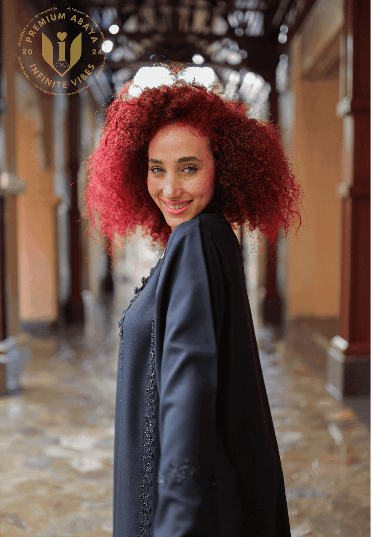 Smiling woman with curly red hair wearing elegant black abaya with detailed embroidery.