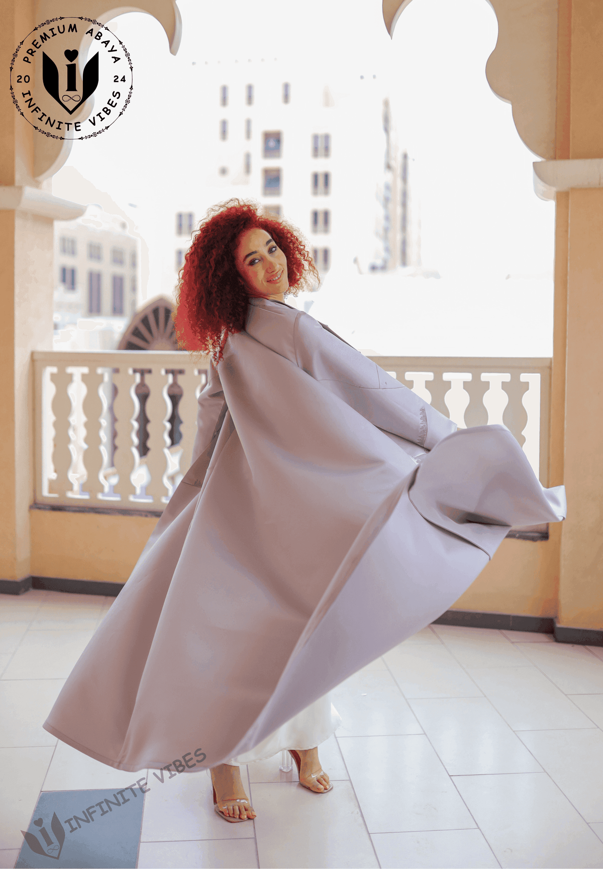 Woman in a flowing grey designer abaya posing on a balcony, elegant and modest fashion