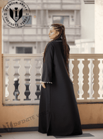 Woman wearing a black designer abaya with white embroidered trim on a balcony, urban background