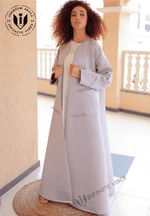 Woman wearing a light grey designer abaya with wide sleeves, standing on balcony