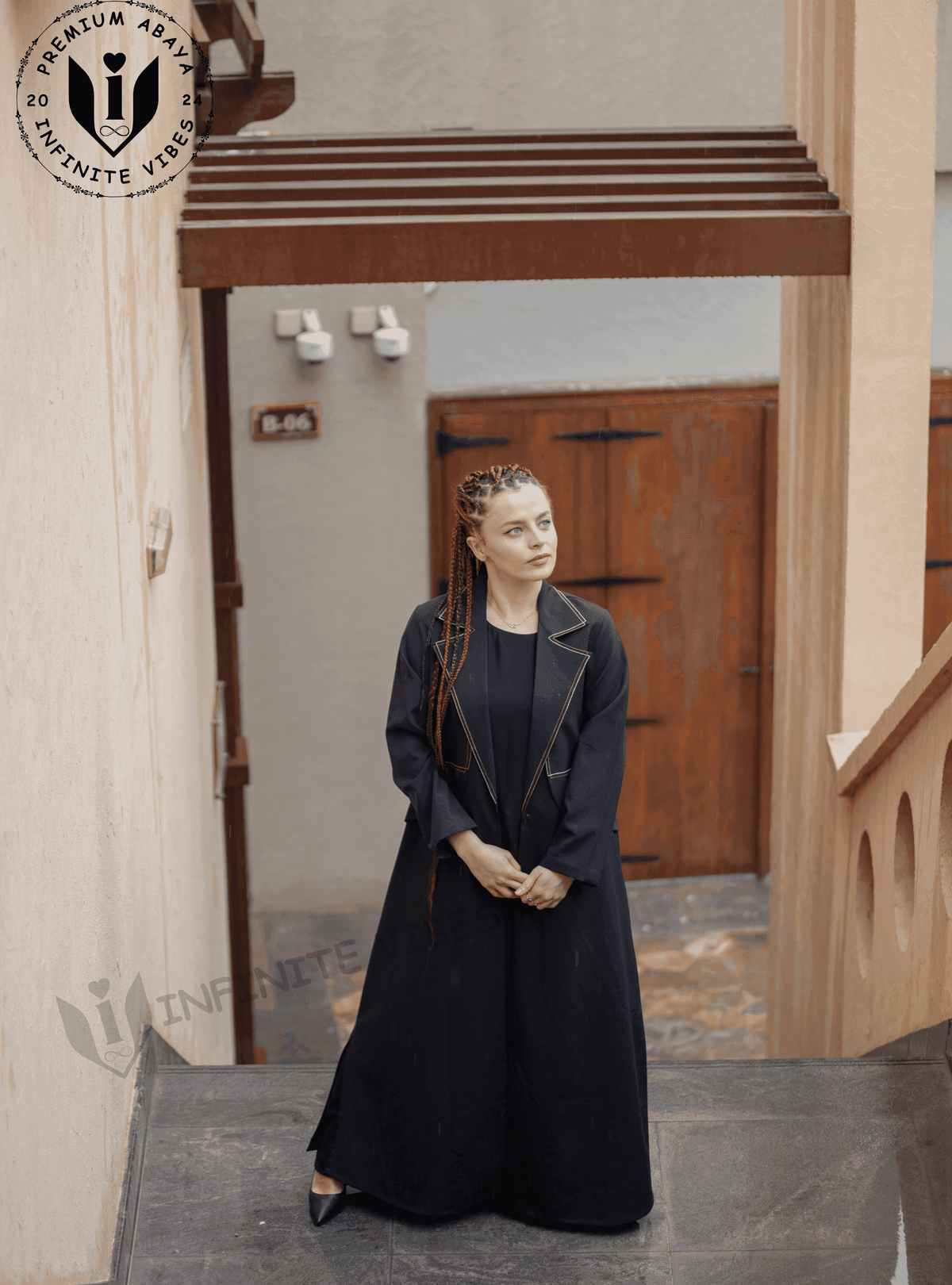 Woman wearing a black designer abaya with gold trim, standing outdoors on stairs
