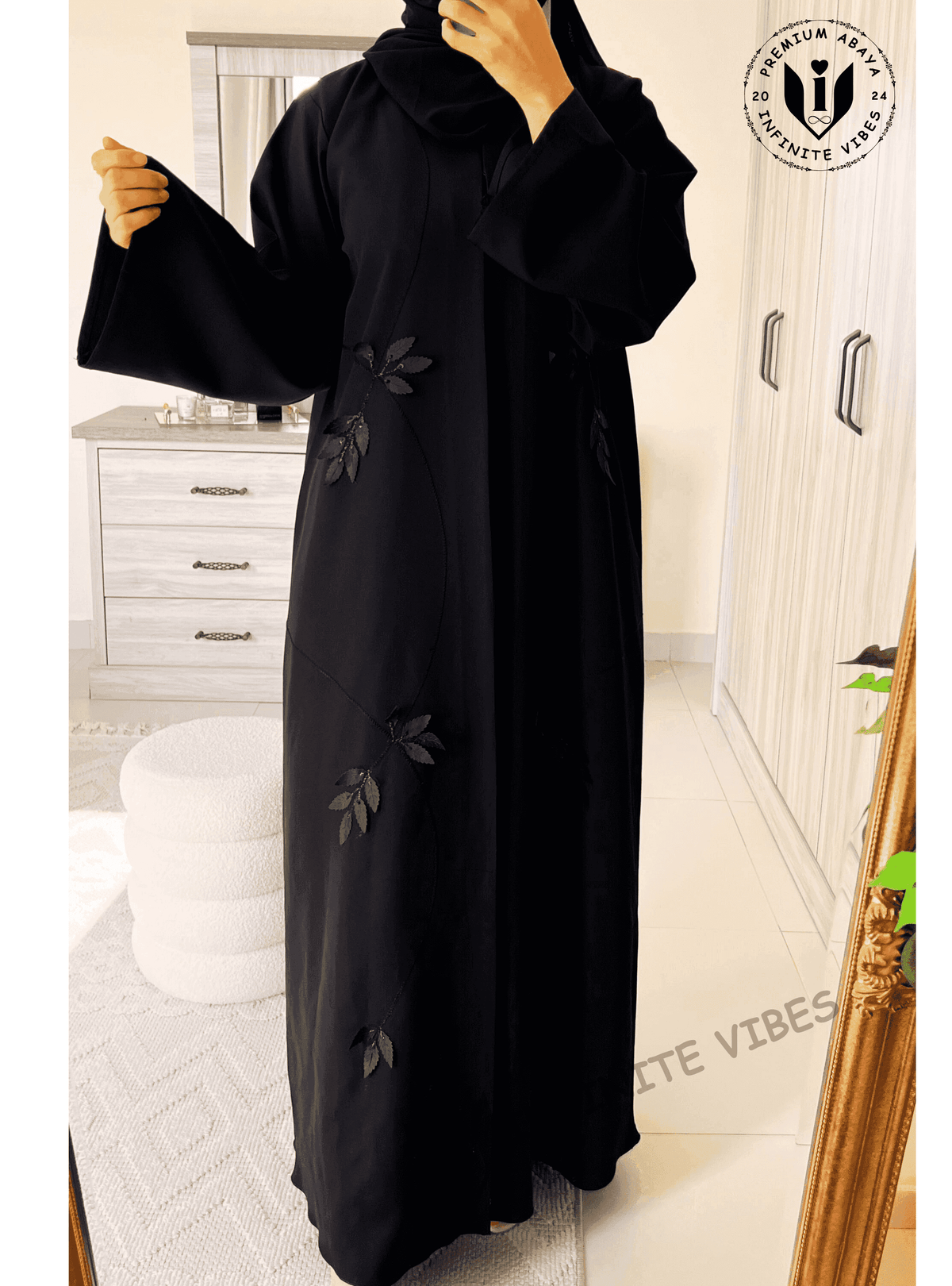 Woman wearing a black designer abaya with leaf embroidery in a modern bedroom