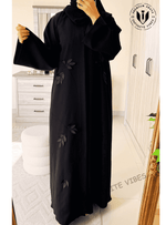 Woman wearing a black designer abaya with leaf embroidery in a modern bedroom