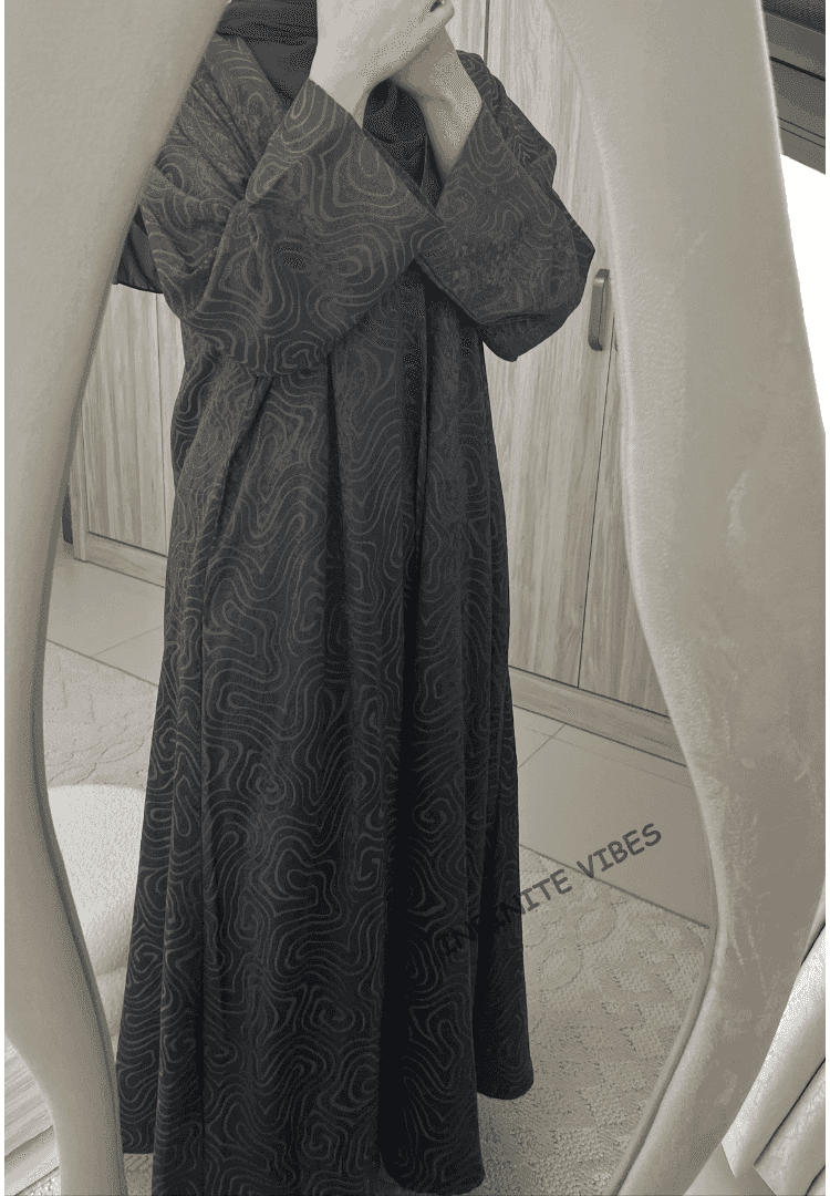 Woman wearing a patterned black abaya with modest long sleeves in front of a mirror