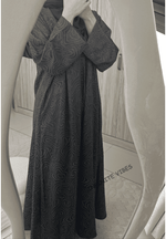 Woman wearing a patterned black abaya with modest long sleeves in front of a mirror