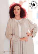 Woman wearing elegant beige abaya with pleated sleeves, modest fashion in bright setting