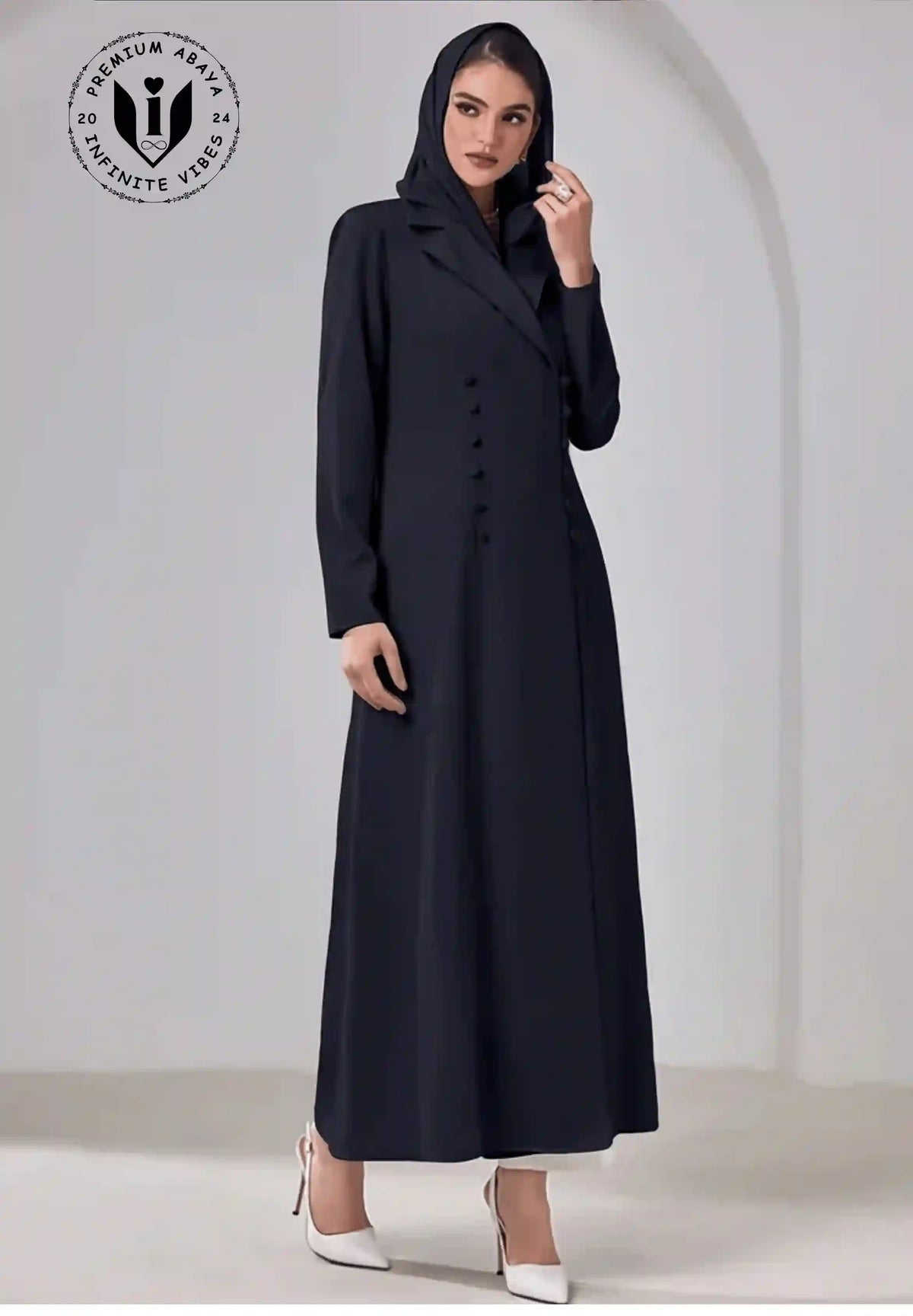 Elegant woman wearing a black buttoned abaya with hood, long sleeves, and white heels.