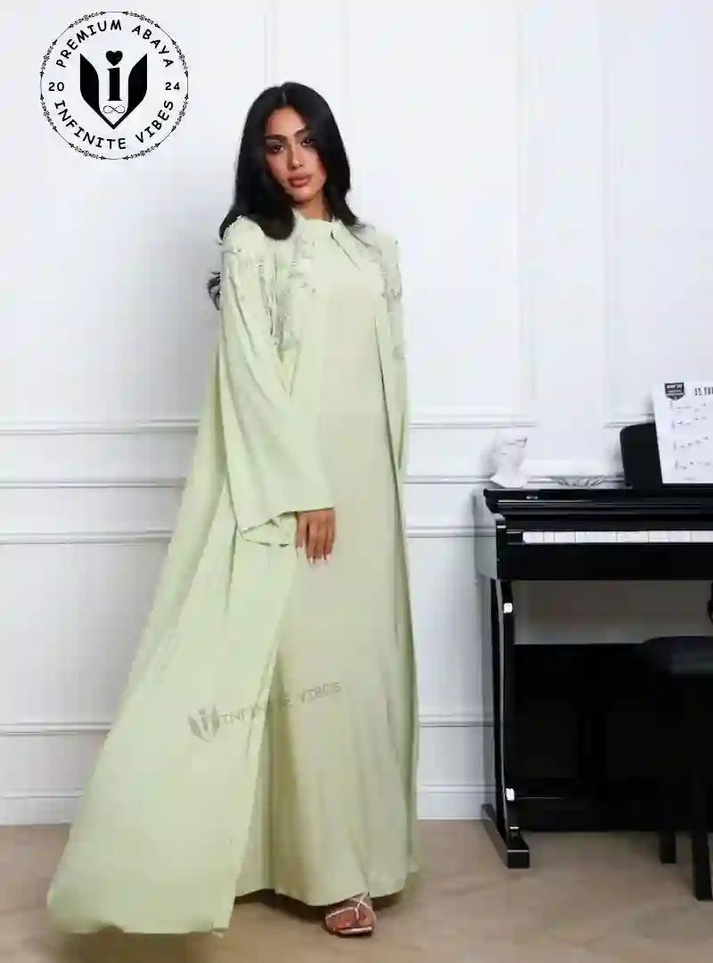 Woman in light green designer abaya with fringe detail, standing indoors by piano
