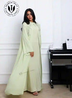 Woman in light green designer abaya with fringe detail, standing indoors by piano