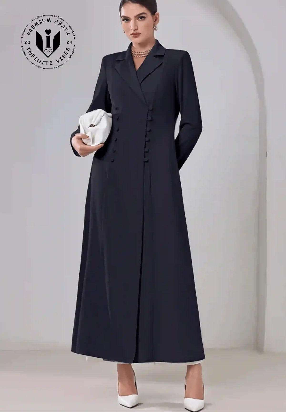 Modern double-breasted black abaya with lapel collar, worn with white heels and clutch.