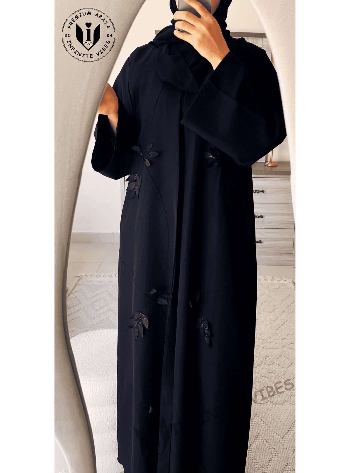 Woman wearing a black designer abaya with floral embroidery, standing in front of a mirror.