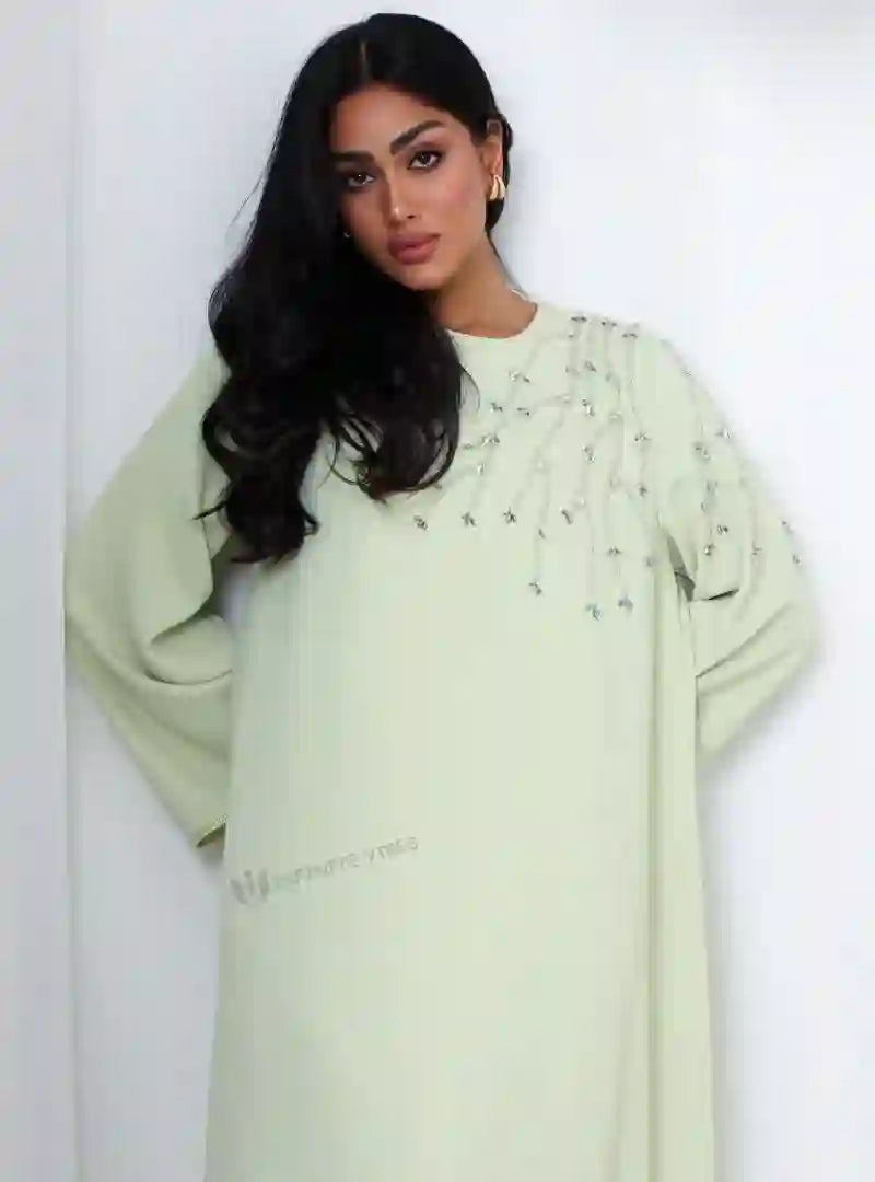 Woman wearing a light green abaya with crystal handwork embroidery, modest fashion style