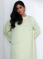Woman wearing a light green abaya with crystal handwork embroidery, modest fashion style