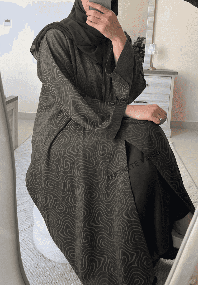 Woman wearing a black abaya with wavy abstract patterns, sitting in a modern room