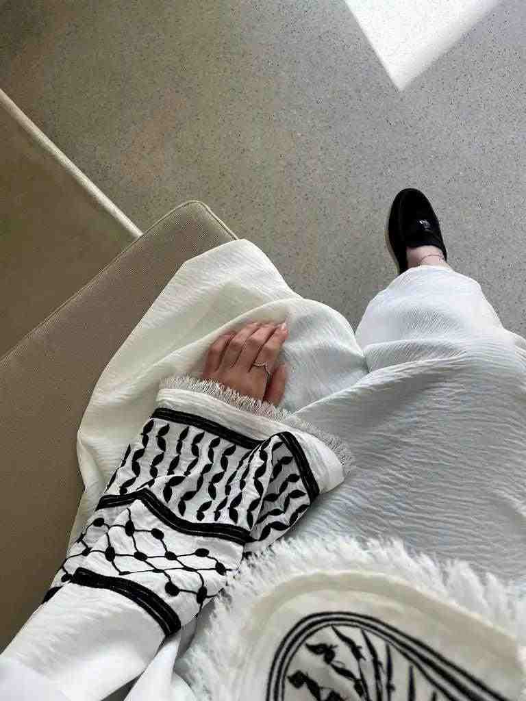 Woman in white open abaya kimono with black embroidery and tassels, black loafer shoes