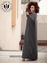 Woman wearing a dark grey designer abaya with button details, standing outdoors.