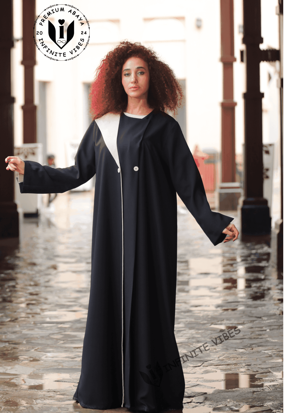 Woman wearing a modern black designer abaya with white accents outdoors on wet stone walkway
