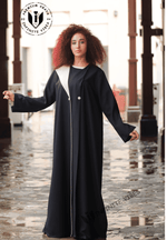 Woman wearing a modern black designer abaya with white accents outdoors on wet stone walkway