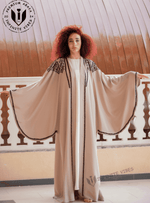 Woman wearing a butterfly sleeve beige embroidered abaya, standing on a balcony