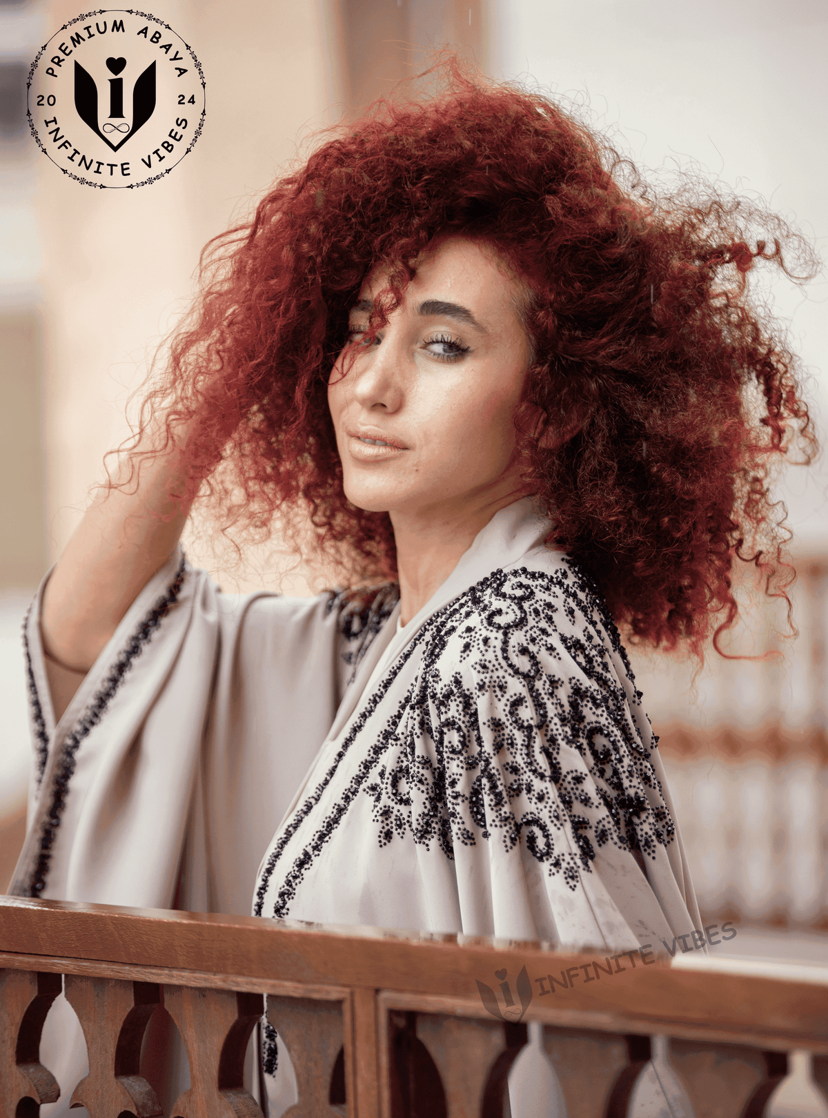 Woman in embroidered butterfly abaya with black beaded detailing, standing by railing