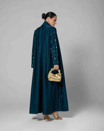 Woman in teal embellished designer abaya holding gold bag and wearing gold heels