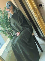 Woman in modern olive green abaya with leaf embroidery, sitting by a mirror indoors