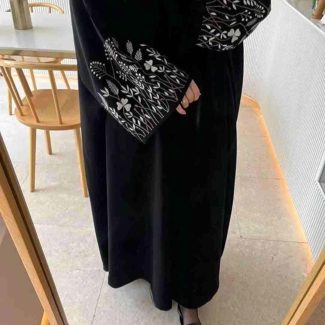 Black abaya with white floral embroidery on sleeves, modest fashion in indoor setting