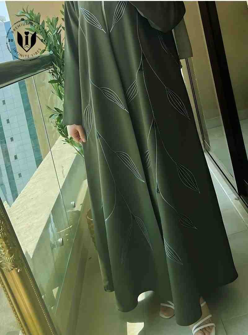 Green embroidery abaya with leaf handwork design, worn on a balcony in sunlight