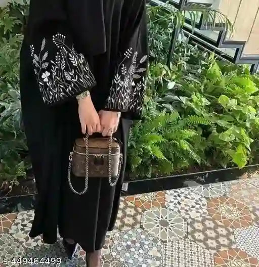 Black abaya with white floral embroidery on sleeves, woman holding a chain handbag, garden background