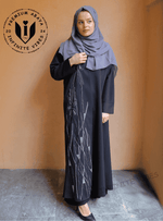 Woman in black handwork embroidered abaya and gray hijab standing against orange wall