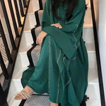 Woman wearing a green embellished abaya sitting on stairs, showcasing modest fashion style