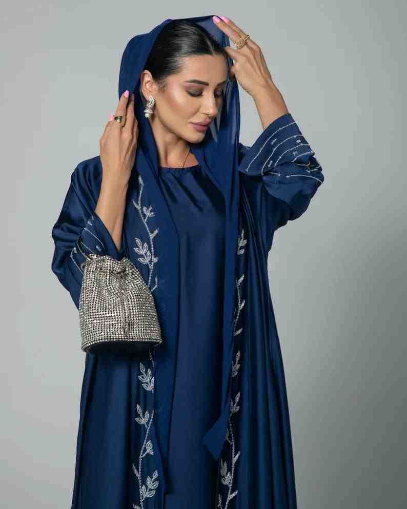Woman wearing a navy blue designer abaya with silver embroidery holding a sparkling bag