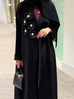 Modern black abaya with floral embellishments, paired with a small black handbag